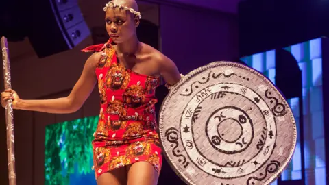 Emmanuel Adegboye / EPA A Miss Universe Nigeria contestant wearing a beaded headband, a red dress with lion print and a silver shield with tribal markings at the pageant in Lagos, Nigeria - Saturday 31 August 2024