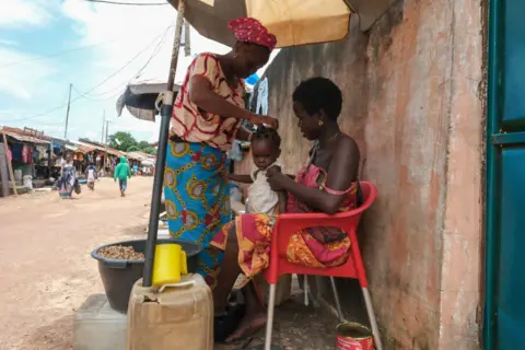 RICCI SHRYOCK / AFP Women tend to a child as they sell peanuts at an outdoor market in Bissau- Monday 30 September 2024