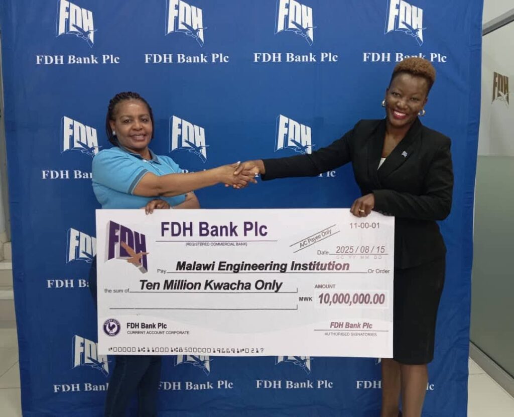 Two women smiling and shaking hands while holding a large ceremonial FDH Bank Plc cheque for Ten Million Kwacha, made out to the Malawi Engineering Institution, against an FDH Bank branded backdrop.
