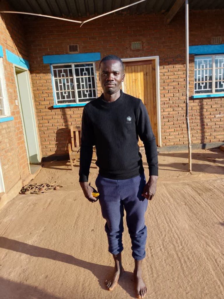 A man in a black sweater and blue trousers standing in front of a brick building
