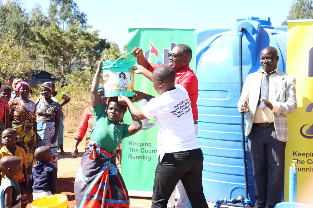 Msimuko in red aiding a woman carry water 002